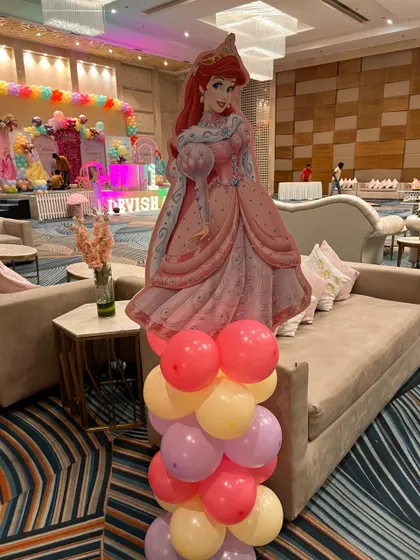A life-sized cutout of Princess Ariel from The Little Mermaid, placed on a balloon base as part of the party decor.
