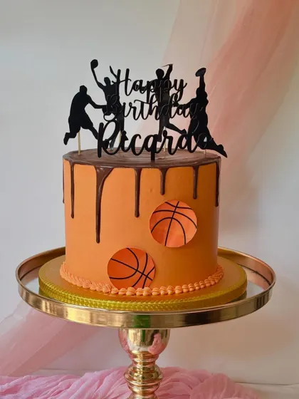An action-packed basketball cake with a chocolate drip. The custom topper shows players in silhouette, making it a dynamic centerpiece for a birthday.