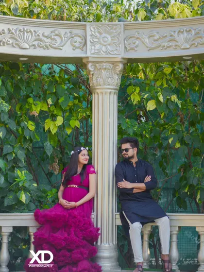 A relaxed portrait of a couple leaning against a white balustrade in a garden setting.