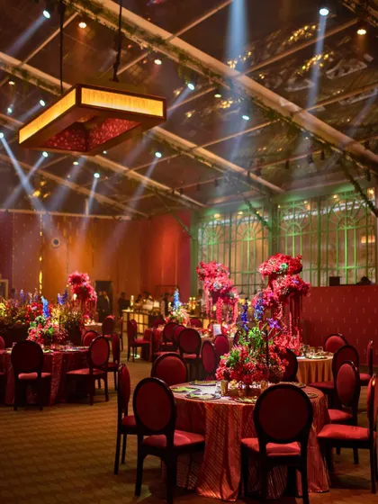 A wide shot of the Sangeet reception, showing the luxurious red and gold table settings under a transparent marquee with a mirrored ceiling.