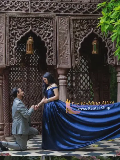 A classic proposal pose. The man is on one knee, and the woman is in a deep blue off-the-shoulder gown with a long trail, creating a truly romantic and memorable photograph.