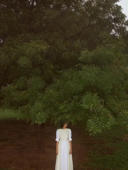 A wide shot from the Sruti Dalmia campaign, placing a model in a simple white dress beneath a large, sprawling tree. The styling and composition create a sense of scale and connection to nature, resulting in a peaceful and poetic image.