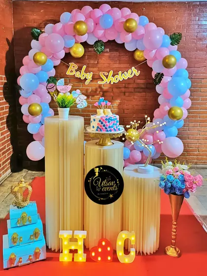 A modern baby shower with a pink and blue balloon ring. The setup includes plinths for the cake and initial marquee letters.