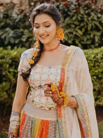 A beautiful portrait of the bride, smiling gently. Her traditional attire, complete with floral jewelry and a braid, is captured in soft, natural light.