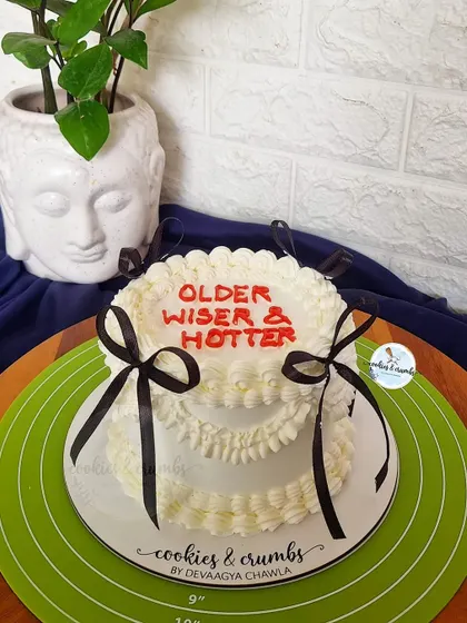 "Older, Wiser & Hotter." A fun and sassy vintage-style cake with piped ruffles and black bows, perfect for a birthday celebration with a sense of humor.