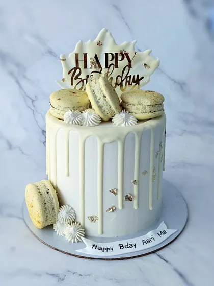 A pretty white cake with no food coloring. This vanilla almond cake is decorated with a white chocolate drip, macarons, and a chocolate shard.