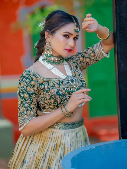 A full-profile shot of a bride in a green and gold lehenga. The makeup is soft yet defined, with a focus on the eyes, making her look poised and elegant.