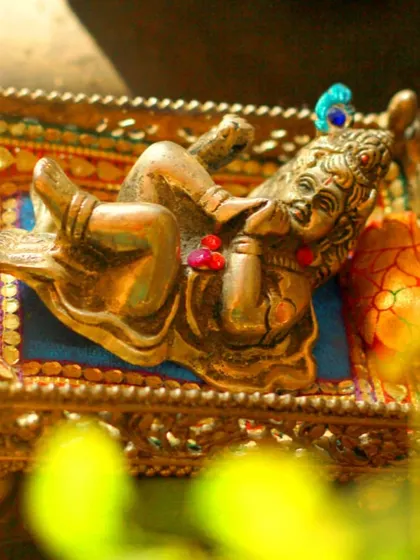 A macro shot of a small brass statue of Lord Krishna, often part of the home altar during a pooja. I focus on these artistic details that add cultural richness to the photo album.
