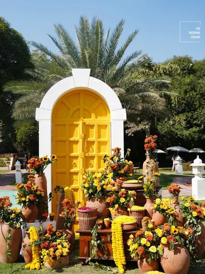 A vibrant photo opportunity with a bright yellow door surrounded by pots of marigolds and other colorful flowers, perfect for a Haldi ceremony.