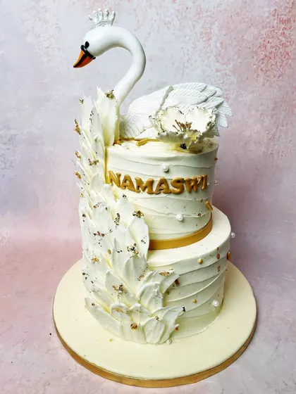 We craft a vision of pure elegance with this two-tiered swan cake. A majestic white swan with a delicate crown glides atop a cake adorned with white feather-like details and gold leaf, creating a breathtaking centerpiece for a sophisticated celebration.