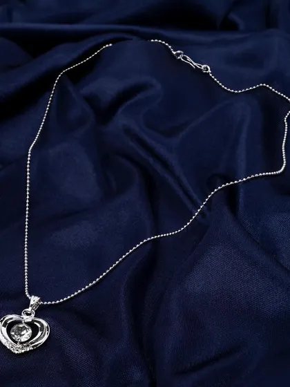A silver heart pendant on a rich, blue satin background. The texture of the fabric adds a sense of luxury and elegance to this jewelry photograph.