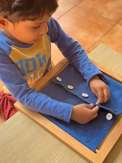 A child masters the skill of buttoning using a dressing frame. These frames isolate a specific skill, allowing the child to practice without the frustration of trying on their own clothes.