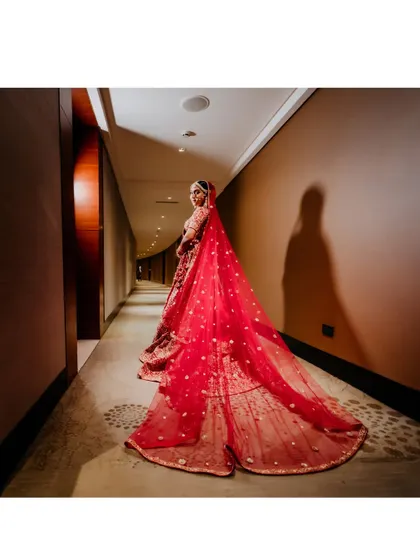 A dramatic shot of the bride from behind, showcasing the full length and beautiful train of her red wedding veil.