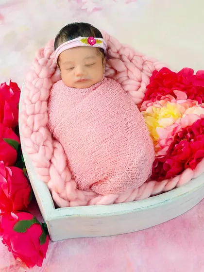 A newborn baby swaddled in pink and nestled in a heart-shaped basket surrounded by flowers. A truly lovely and artistic way to capture your new love.