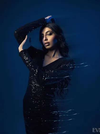 A powerful pose with the model's arms raised, enhanced by motion blur light streaks. The dark blue background makes the sequined dress and the light effects pop.