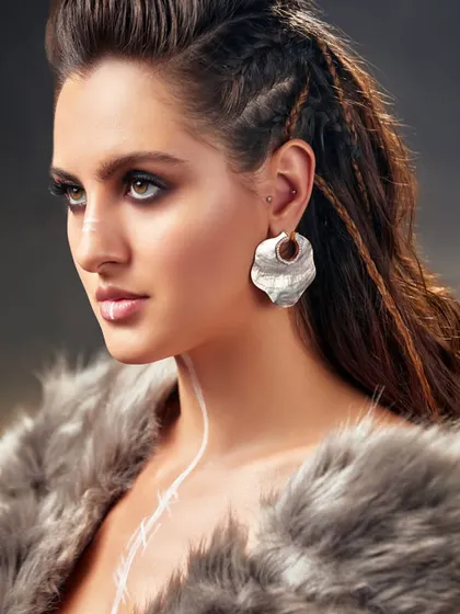 A close-up beauty shot from the Pure Facets campaign, highlighting the unique hammered-metal earring and fierce makeup.
