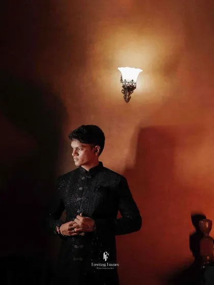 A dramatic portrait of the groom in a dark sherwani, illuminated by a single light source.