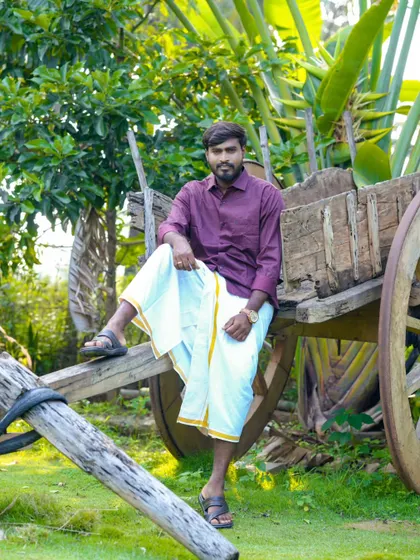 A solo portrait of the groom-to-be in traditional South Indian attire, posing with a rustic bullock cart.