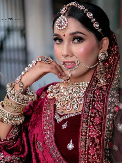 A close-up portrait where the bride's hand, adorned with a hath phool, frames her face. This composition emphasizes her striking makeup and the detailed craftsmanship of her jewellery.