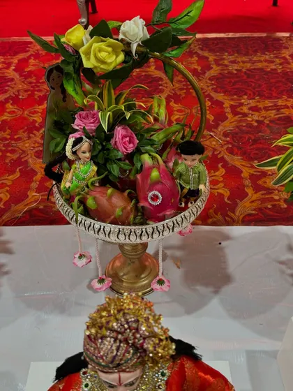 A creative fruit arrangement featuring dragon fruits and small dolls. The basket is decorated with a floral arch, making it a unique and eye-catching piece.