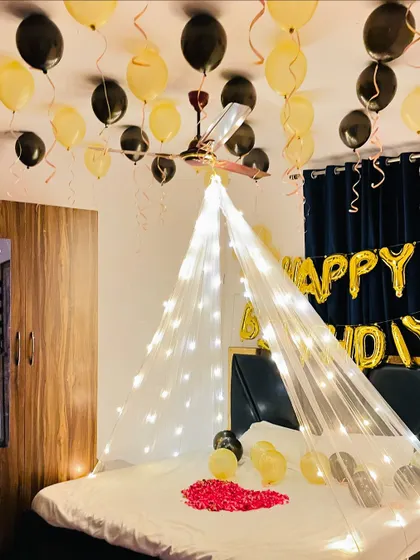 Another angle of the black and gold room setup, with a heart of rose petals on the bed and balloons with ribbons hanging from the ceiling.