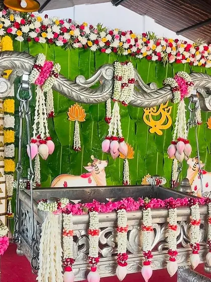 A close-up view of an ornate silver cradle set against a backdrop of banana leaves and flowers. This setup is perfect for a combined Seemantham and naming ceremony.