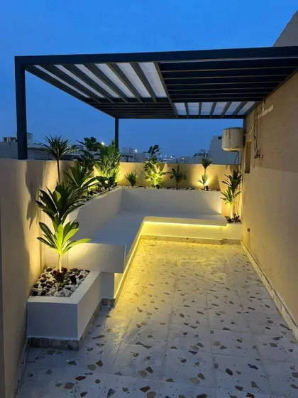 A narrow rooftop space transformed into a stylish lounge with built-in L-shaped seating and planters. The evening lighting creates a chic and intimate atmosphere.
