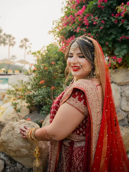 The final look. A stunning bride in a red and gold lehenga, with a classic red lip and glowing skin, ready for her big day.