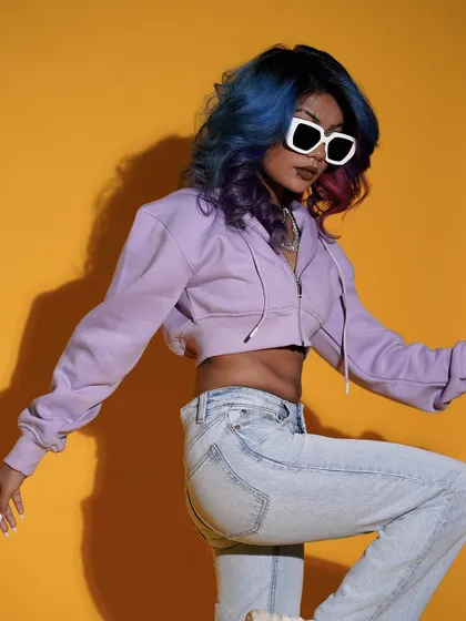 A dynamic action pose that brings energy to the frame. The model's movement and colorful hair pop against the yellow backdrop, creating a fun and youthful image perfect for a Gen Z-focused brand.