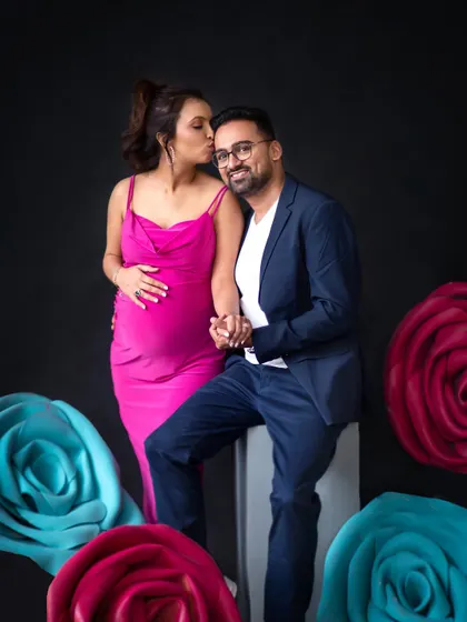 A sweet kiss on the cheek surrounded by colorful paper flowers. This studio setup adds a touch of whimsy and romance to the maternity session.