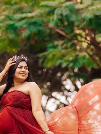 A regal portrait of an expectant mother in a red gown and crown, with the wind catching the fabric. The natural outdoor setting provides a beautiful backdrop for this powerful shot.