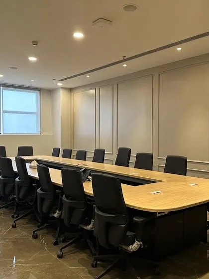 A wider perspective of the conference room, showing the full length of the table and seating arrangement. The recessed linear lighting in the ceiling ensures the entire room is evenly illuminated.