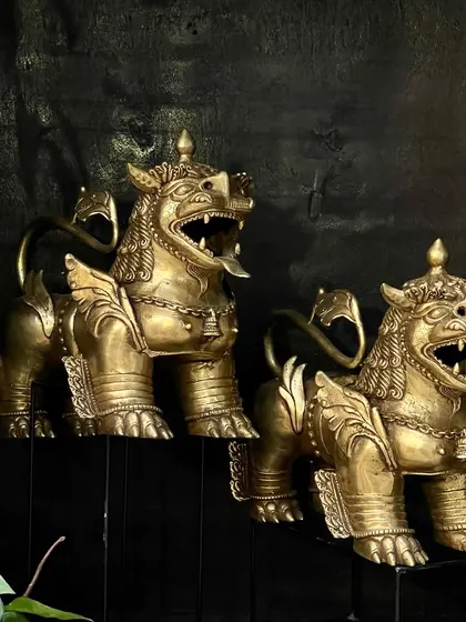 A full view of the pair of brass Buddhist temple lions. Placed on stands, they command attention and serve as guardians of the abode, keeping evil at bay.
