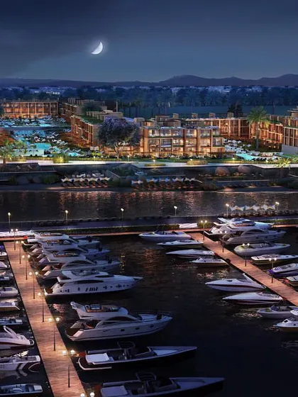 A night-time aerial view of the coastal marina development. The illuminated buildings, streets, and docks create a stunning visual that highlights the vibrant nightlife of the community.