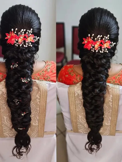 A thick, fishtail braid adorned with bright orange floral accessories. This is a vibrant and unique hairstyle for a pre wedding event or a modern bride.