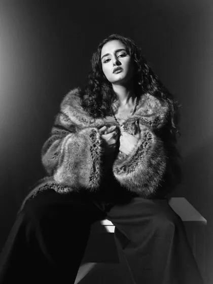A glamorous black and white portrait. The high-contrast lighting emphasizes the texture of the faux fur coat and the model's confident expression.