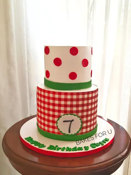A fun two-tier cake with a red and white gingham pattern on the bottom tier and polka dots on top. A playful design perfect for a pizza party or picnic-themed event.