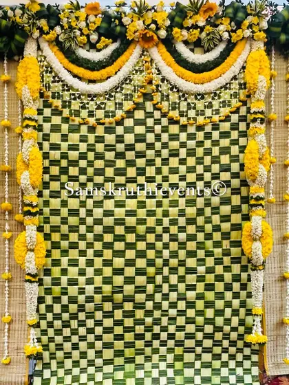 A classic backdrop with a checkerboard pattern of woven leaves. The hanging garlands of marigold and jasmine add a traditional and fragrant element to the decor.