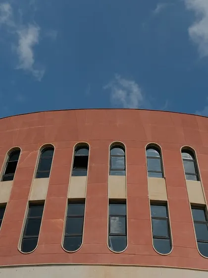 A detail of the curved red sandstone wall and its rhythmic pattern of arched windows. This architectural feature defines the building's unique circular form.