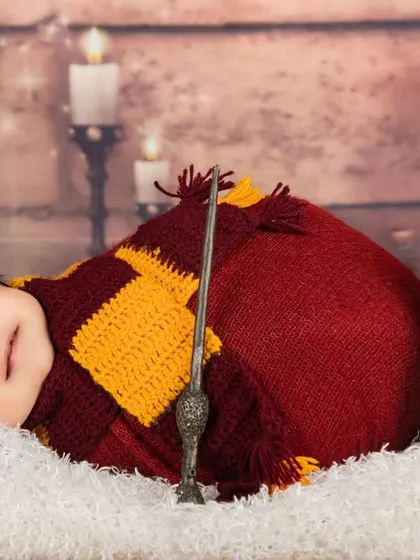 Dreaming of magic. This sleeping newborn is dressed in a Gryffindor-colored wrap, complete with a tiny wand and a knitted owl friend.