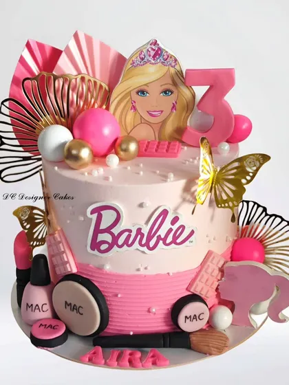 A modern and stylish Barbie cake for a 3rd birthday. This design incorporates trendy elements like paper fans and edible makeup items from MAC, giving it a chic and fashionable look.