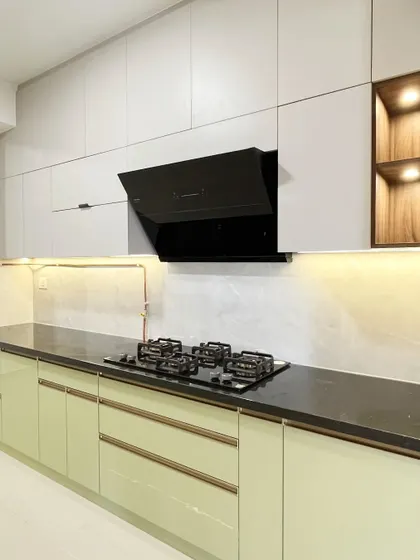 A cheerful kitchen in pista green and white, with sleek wooden open units for display. The black quartz countertop provides a modern, high-contrast element.