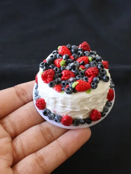 A beautiful miniature berry chantilly cake, topped with tiny, realistic raspberries and blueberries.
