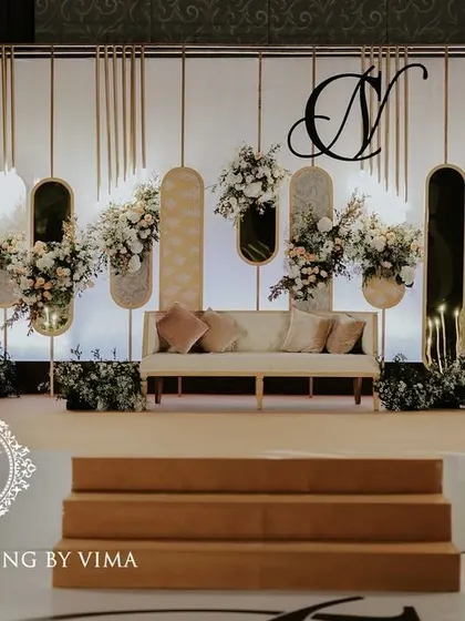 A classic and elegant reception setup symbolizing everlasting love. The stage features a modern, minimalist backdrop with custom monograms, floral arrangements, and soft lighting.