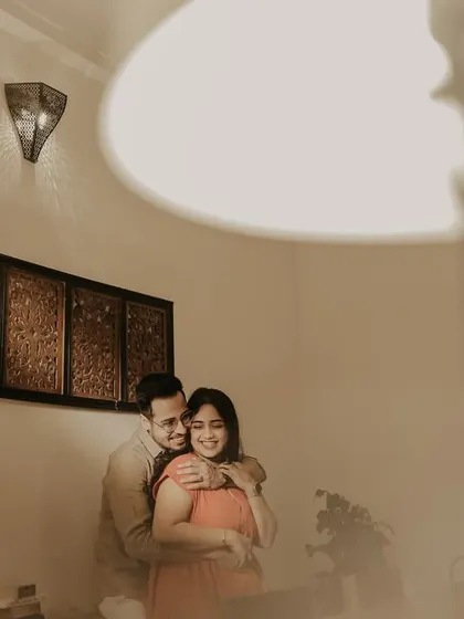 A warm and joyful indoor portrait with the groom embracing the bride from behind. The soft lighting from the lamps creates a cozy and intimate atmosphere for this candid moment.