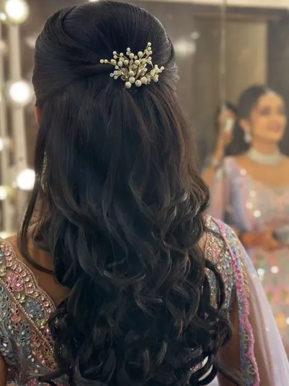 A half-updo with soft waves, accessorized with a delicate pearl and crystal clip. The reflection in the mirror shows the happy client.
