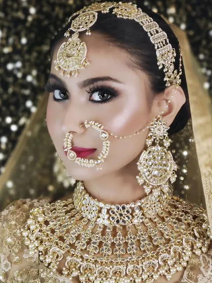 A close-up of a heavy, champagne-gold bridal set with intricate details and pearl accents. The matching nath and large earrings complete this stunning look.