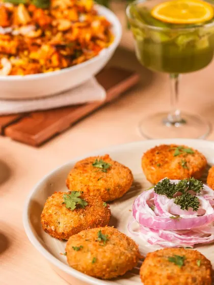 A close-up perspective of crispy appetizers, with a refreshing drink and another dish blurred in the background. This composition creates depth and context, showing a complete meal setting.