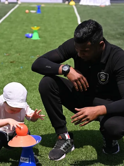 A coach from our sports program partner helps a toddler with a balancing activity.