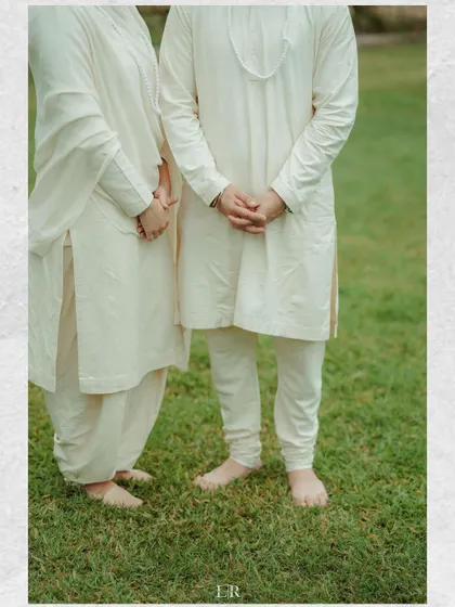A detail shot of a couple's lower half, showing them standing barefoot on the grass in their elegant white outfits.